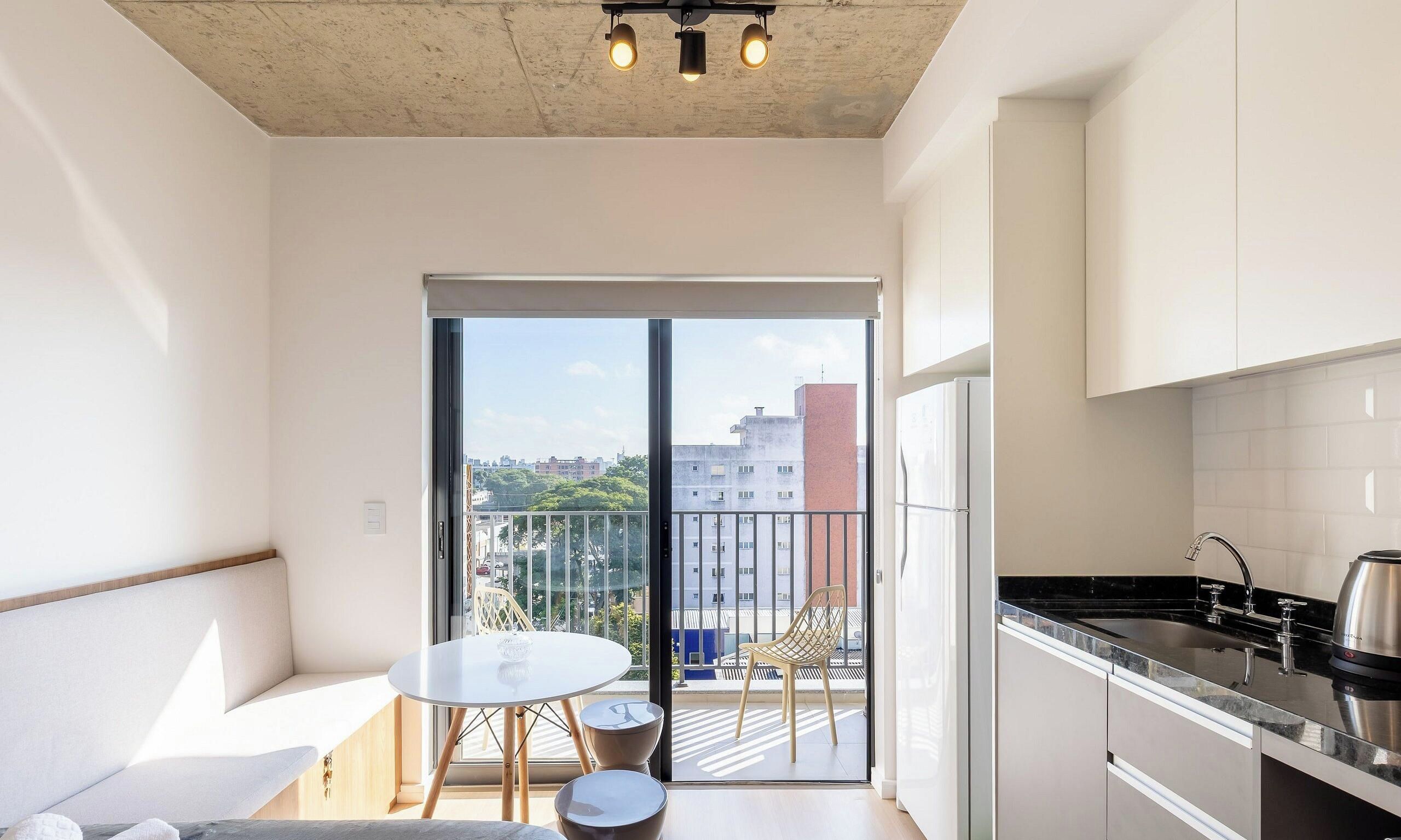 Un appartement moderne doté d’un balcon, d’une cuisine avec un évier en acier inoxydable et d’un coin repas comprenant une table et des chaises.