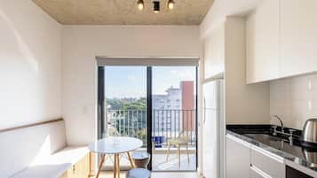 Un appartement moderne doté d’un balcon, d’une cuisine avec un évier en acier inoxydable et d’un coin repas comprenant une table et des chaises.