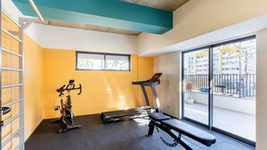 A gym with exercise equipment, a bench, and a window with a view of buildings.