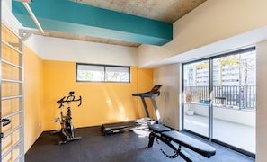 Een fitnessruimte met trainingsapparatuur, een bank en een raam met uitzicht op gebouwen.