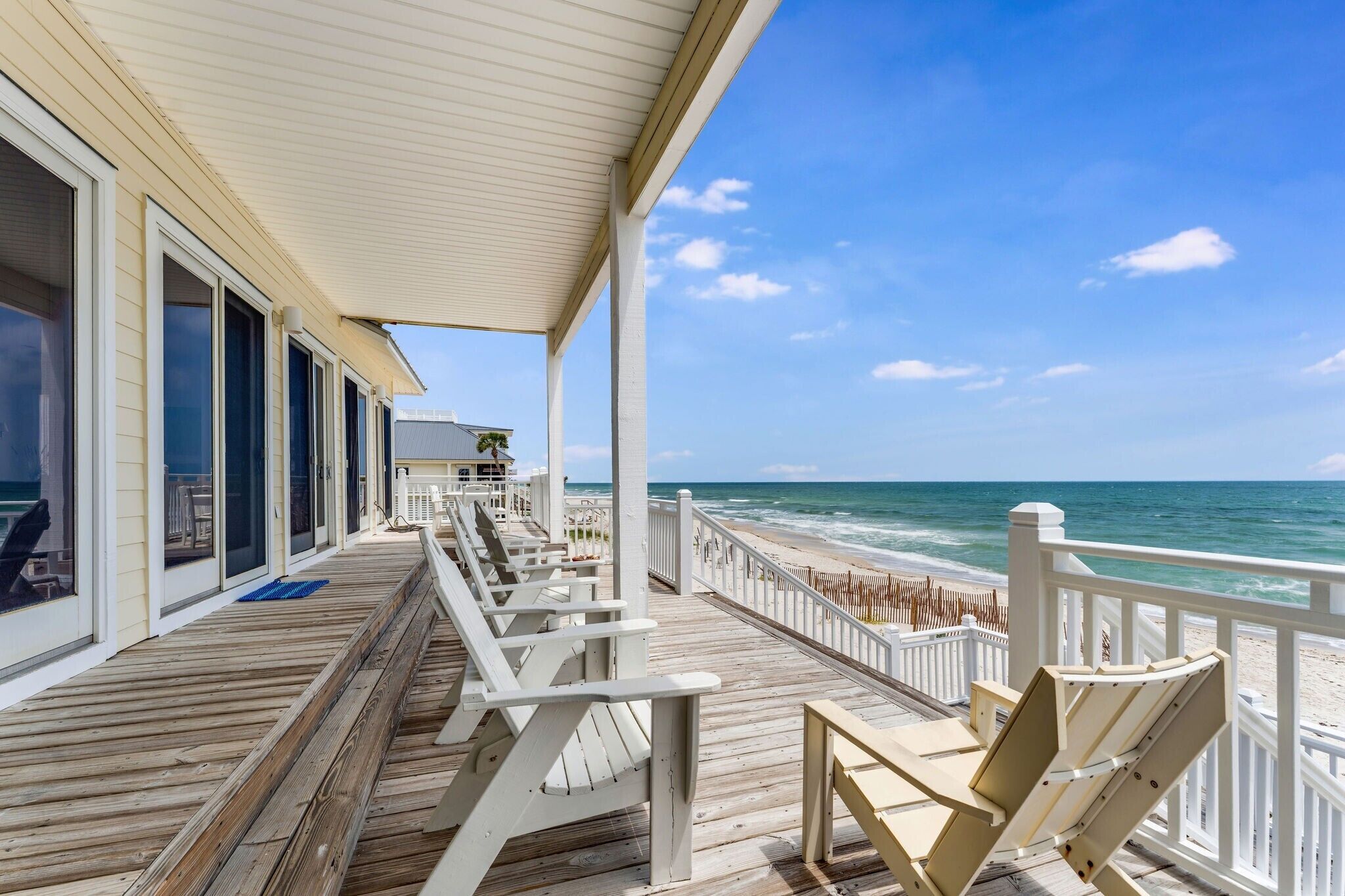 A wooden deck with white railings, overlooking a beach and ocean.