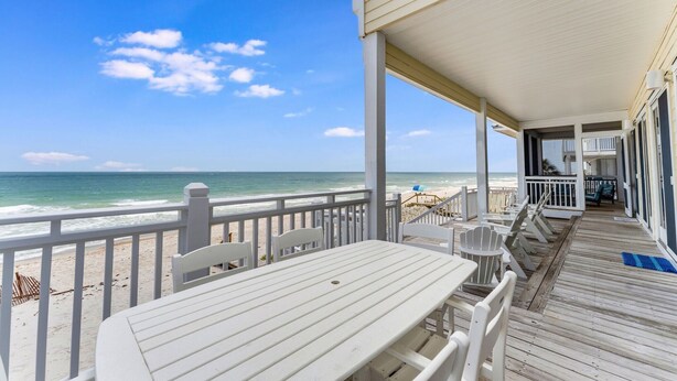 Een terras aan het strand met witte meubels, uitzicht op de oceaan en een gebouw met een balkon.
