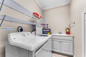 A laundry room with a front-loading washer, a sink, and a fire extinguisher. - Sea Glass, Beach Front, Renovated, Community Pools, Beach Gear Credit! (St. George Island)