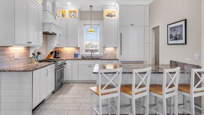 Een moderne keuken met witte kasten, een centraal eiland met barkrukken en een raam met jaloezieën.