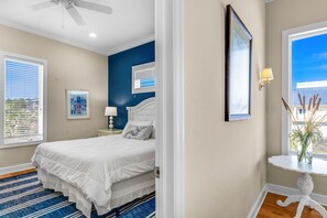 A bedroom with a bed, a nightstand, a lamp, a framed mirror, and a window with a view. - Sea Glass, Beach Front, Renovated, Community Pools, Beach Gear Credit! (St. George Island)