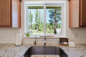 Eine Küche mit Spüle aus Edelstahl, einem Fenster mit Blick auf Bäume und einer Arbeitsplatte mit Wasserkocher und Gläsern.