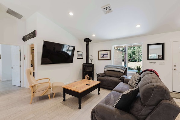 Una sala de estar con televisor de pantalla plana, chimenea, sofá, mesa de centro y una puerta que da a otra habitación.