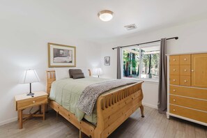 A bedroom with a wooden bed, bedside tables, a wardrobe, and a window with a view of trees.