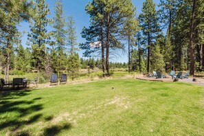 A grassy outdoor area with a picnic table and chairs, surrounded by tall pine trees.