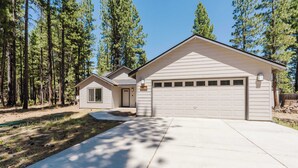 A two-story house with a garage, surrounded by tall pine trees.