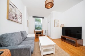 Ein modernes Wohnzimmer mit grauem Sofa, einem weißen Couchtisch, einem Flachbildfernseher auf einem Holzboden und einem Essbereich mit Tisch und Stühlen.