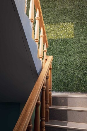 A wooden staircase with a dark wall and a green hedge in the background.