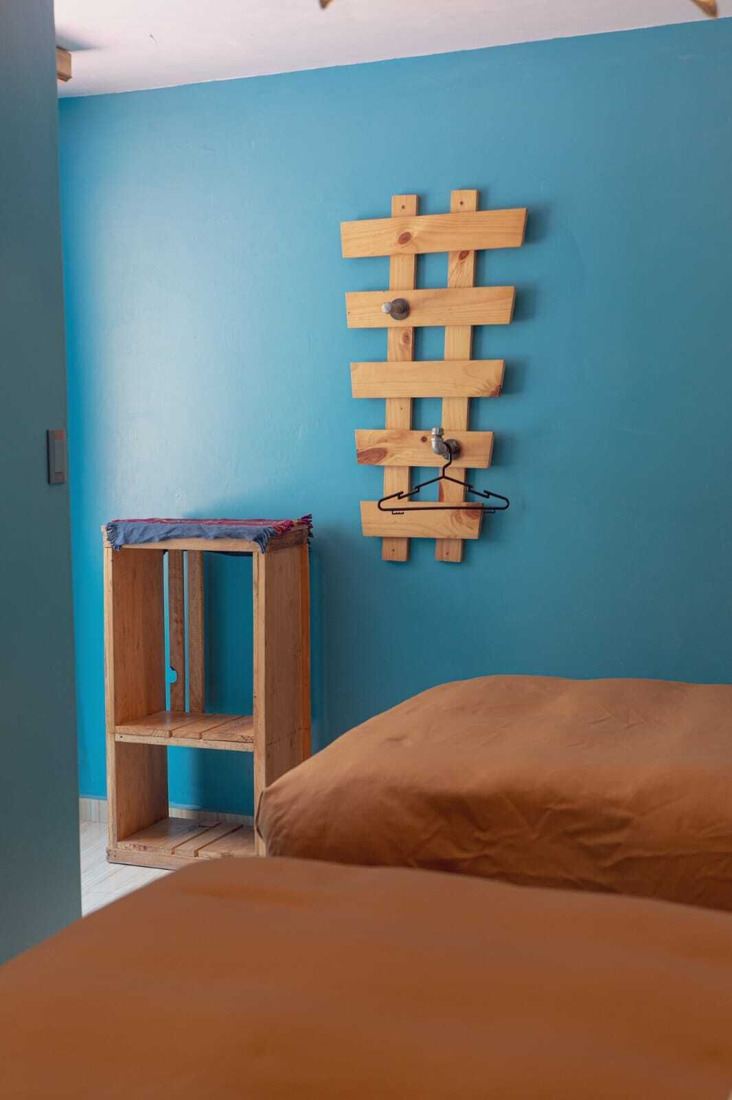 Ein Zimmer mit blauer Wand, einem Holzgestell mit Kleiderhaken und einem Bett mit brauner Bettdecke.