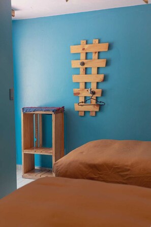 A room with a blue wall, a wooden rack with a hanger, and a bed with a brown cover.