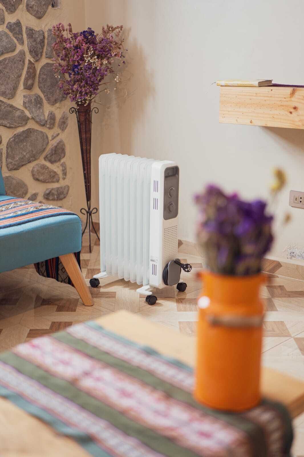 Et værelse med en radiator, en seng med et mønstret sengetæppe, trægulv og en vase med blomster.