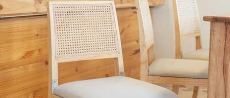 A wooden chair with a woven backrest and cushioned seat, placed on a herringbone-patterned floor.