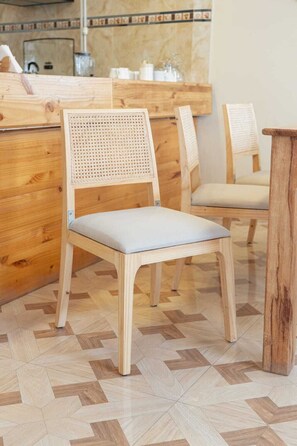 Una silla de madera con respaldo trenzado y asiento acolchado, sobre un piso con diseño de espiga.