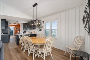 Une cuisine moderne dotée d’un îlot central, de murs recouverts de panneaux blancs et d’un coin repas avec des chaises blanches.