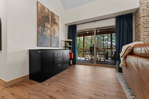 Ein modernes Wohnzimmer mit einer schwarzen Unterhaltungsecke, einem Ledersofa und einer Glasschiebetür, die zu einem Außenbereich führt.