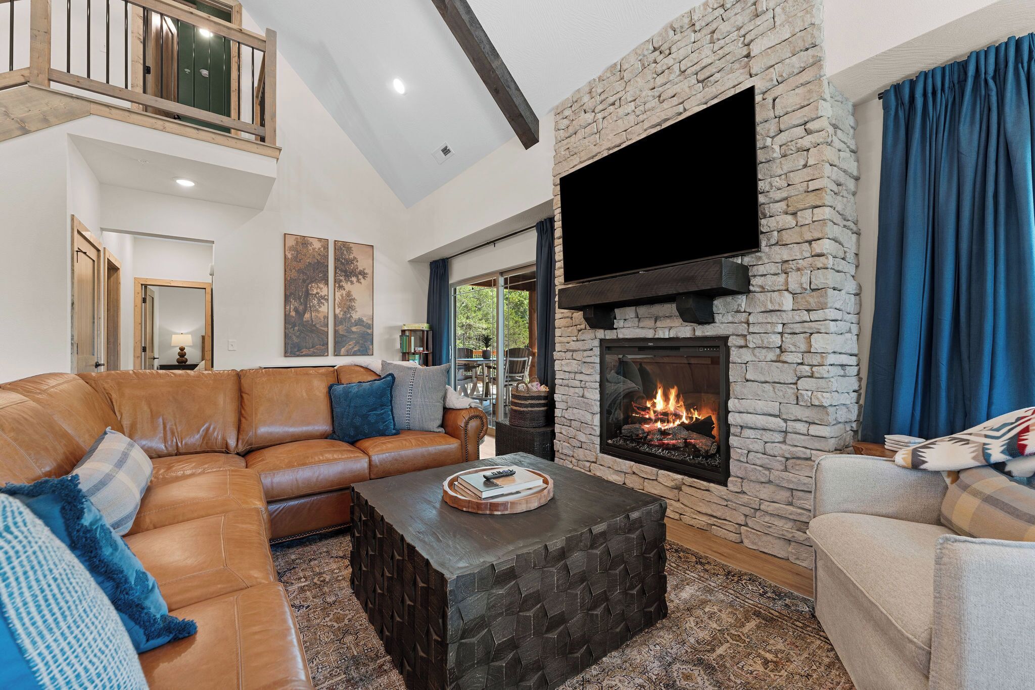 A living room with a stone fireplace, leather sofa, and a flat-screen TV mounted above it.