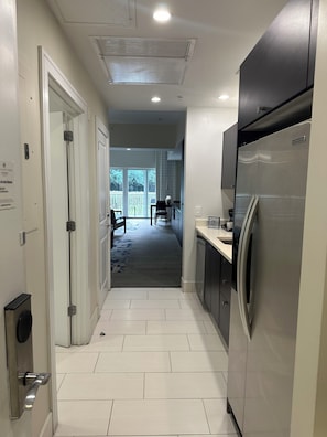 A narrow hallway with a kitchen area on the right, featuring a stainless steel refrigerator and a coffee maker on the counter. - Modern Luxury one bedroom apartment in Doral Florida! (Doral)