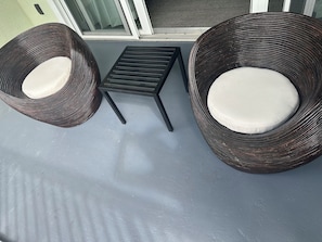 Zwei Korbstühle mit Kissen und ein kleiner schwarzer Tisch auf einem Balkon.