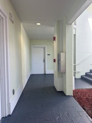 Ein Flur mit einer Tür am Ende, einer Überwachungskamera und einem Rauchmelder an der Wand.