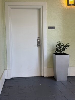 A white door with a push button lock, a potted plant, and a light fixture on the wall. - Modern Luxury one bedroom apartment in Doral Florida! (Doral)