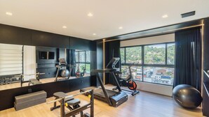 A modern gym with exercise equipment, a large mirror, and a view of a cityscape through large windows. - Studio w/ Grill Near Oktoberfest Eln0905 (Blumenau)