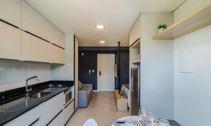 A modern kitchen with a black countertop, stainless steel appliances, and a grey sofa in the adjacent living area. - Studio w/ Grill Near Oktoberfest Eln0905 (Blumenau)