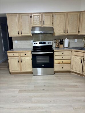 A kitchen with wooden cabinets, a stainless steel range hood, a black stove, and a countertop with a knife block and paper towel holder. - Stylish and cozy retreat, Utica (Utica)