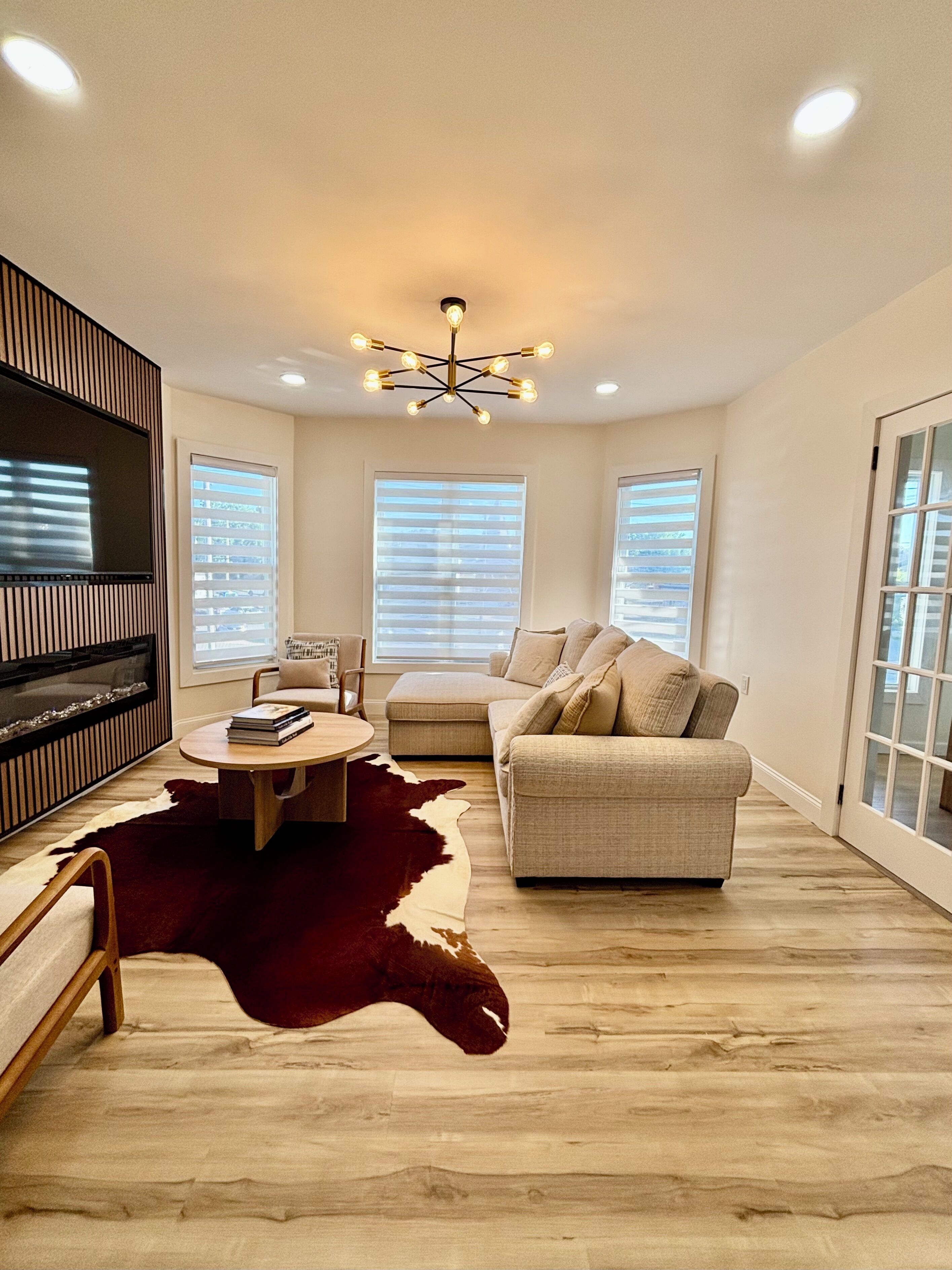 A modern living room with a flat-screen TV, a round coffee table, a sofa, and a large window with blinds.