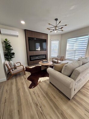 A modern living room with a flat-screen TV, a fireplace, a sofa, and a coffee table. - Stylish and cozy retreat, Utica (Utica)