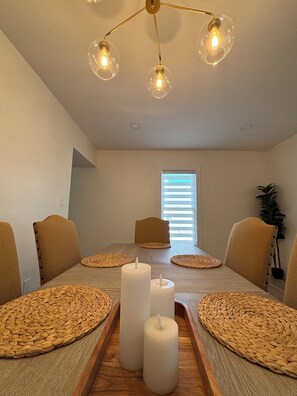 A dining room with a wooden table, woven placemats, candles, and a modern chandelier. - Stylish and cozy retreat, Utica (Utica)