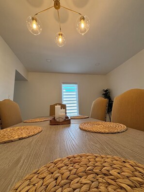 Un comedor con mesa de madera, individuales tejidos y una araña.