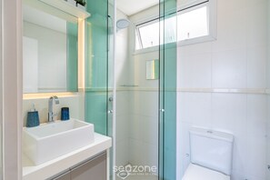 Een moderne badkamer met een douchecabine van glas, een witte wastafel en een toilet.