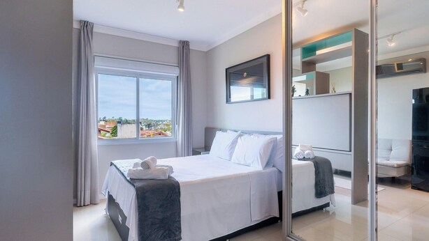 A modern hotel room with a large bed, a view through a glass door, and a mirror reflecting the room. - Complete Studio 900 m From Lagoa Ecm0206 (Florianópolis)