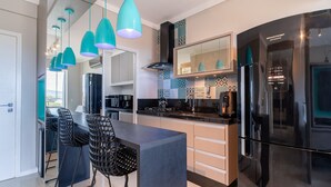 A modern kitchen with a black refrigerator, teal pendant lights, and patterned backsplash. - Complete Studio 900 m From Lagoa Ecm0206 (Florianópolis)