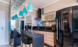 Een moderne keuken met een zwarte koelkast, smaragdgroene hanglampen en een decoratieve spatwand.