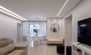 Uma sala de estar moderna com sofá, TV e área de refeições com cadeiras e mesa.