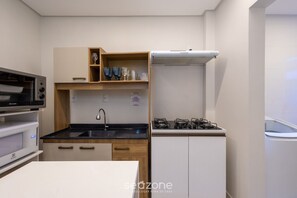 Cozinha compacta com micro-ondas, forno, pia e fogão a gás.