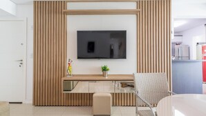 Una sala moderna con televisor de pantalla plana montado en una pared de paneles de madera, una mesita con una planta en maceta y un sillón de mimbre.