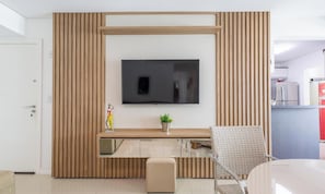Una sala de estar moderna con un televisor montado en una pared de paneles de madera, una mesa de centro de vidrio, un sofá color beige y una silla de mimbre.