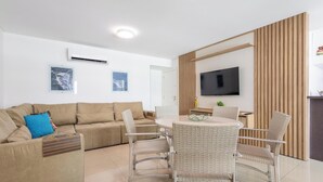 Un salón moderno con sofá, mesa de comedor, sillas, televisor de pantalla plana y obras de arte en las paredes.