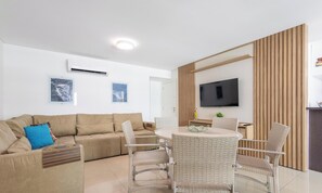 Un salón moderno con sofá, mesa de comedor, sillas, televisor de pantalla plana y obras de arte en las paredes.