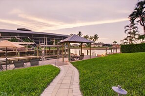 Ein Anwesen am Wasser mit überdachter Terrasse, Sitzgelegenheiten im Freien und einem Weg zum Wasser.