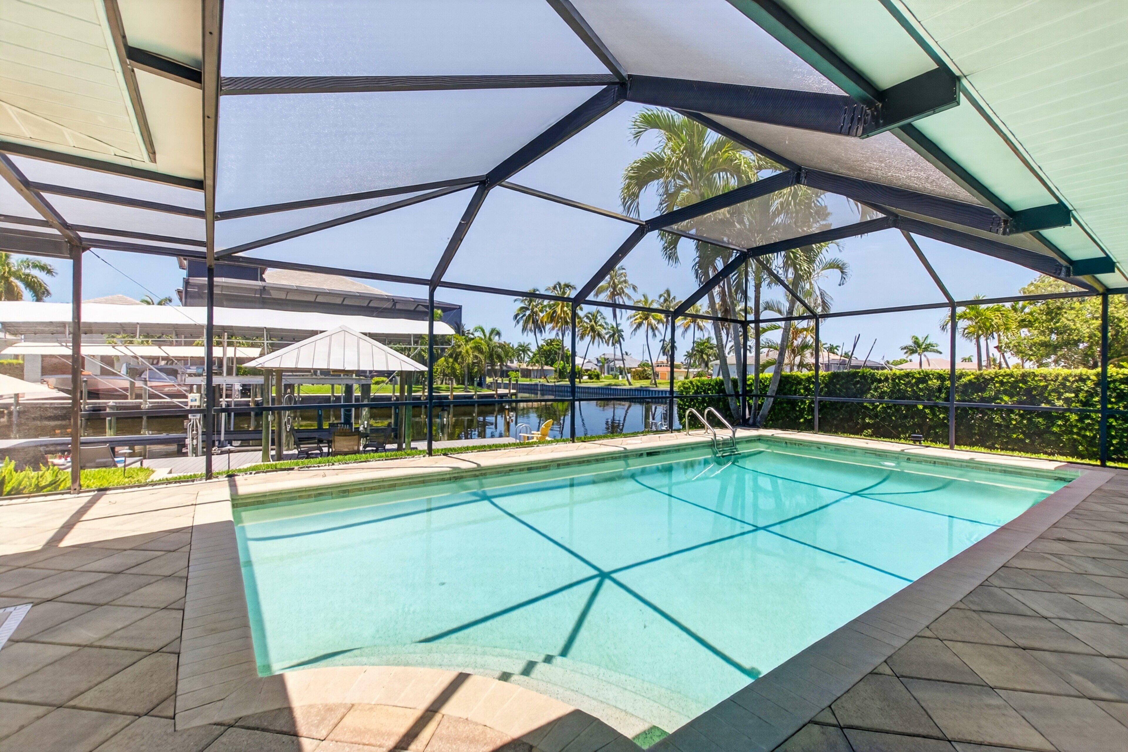 Una piscina con superficie de agua azul cristalina, rodeada por una zona cubierta con estructura de metal de diseño geométrico.
