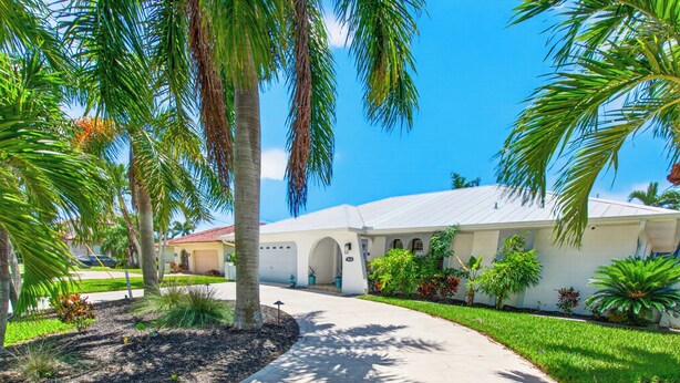 A residential building with a paved driveway, palm trees, and a clear blue sky. - VILLA RIVERSIDE– HEATED POOL | GULF ACCESS | BOAT RENTAL + TOURS VOUCHER INCL. (Cape Coral)