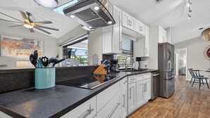 A modern kitchen with white cabinetry, a black countertop, and stainless steel appliances. - VILLA RIVERSIDE– HEATED POOL | GULF ACCESS | BOAT RENTAL + TOURS VOUCHER INCL. (Cape Coral)