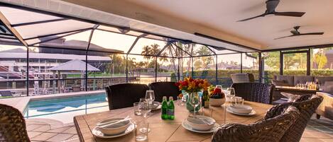 A dining area with a table set for two, overlooking a swimming pool and a view of palm trees.